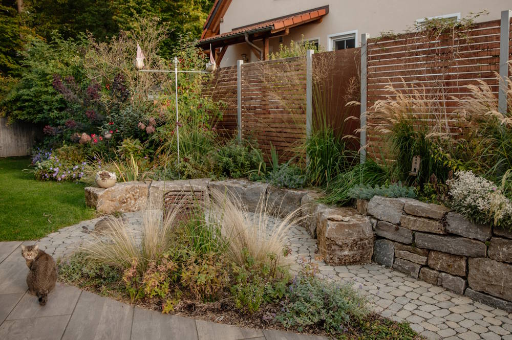 Individuell gestalteter Garten mit Natursteinmauer, strukturierter Bepflanzung und Wegeführung
