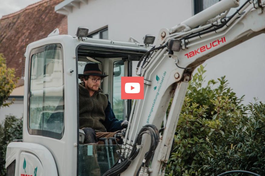 Gartenbauer steuert Bagger bei Arbeiten im Garten und Landschaftsbau