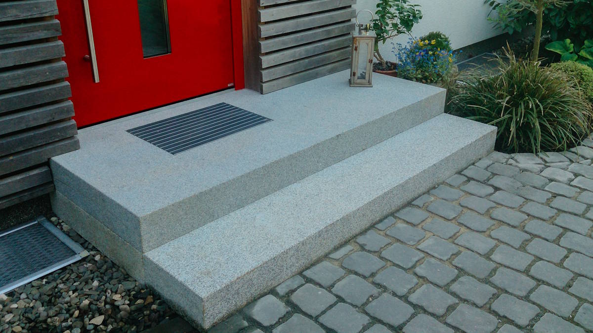 Eingangsbereich eines Hauses mit gepflasterter Fläche und roter Haustür